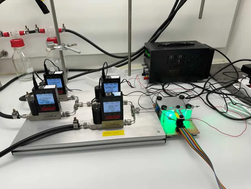 Installation avec quatre unités de dosage (à gauche), qui alimentent des mélanges de gaz à teneur variable en oxygène dans la chambre de mesure éclairée en vert avec le capteur (à droite)